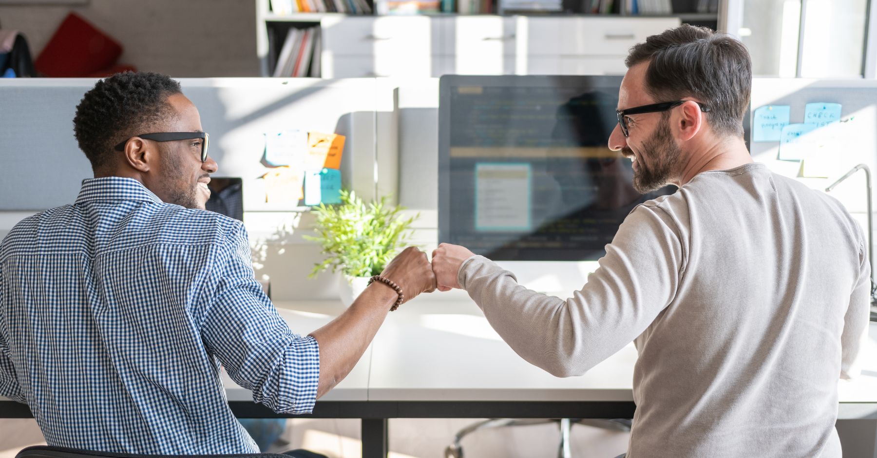 Zwei Männer geben sich fist bump. Sie blicken sich lächelnd an, weil sie zufrieden über das Thema Gesundheit im Unternehmen gesprochen haben.